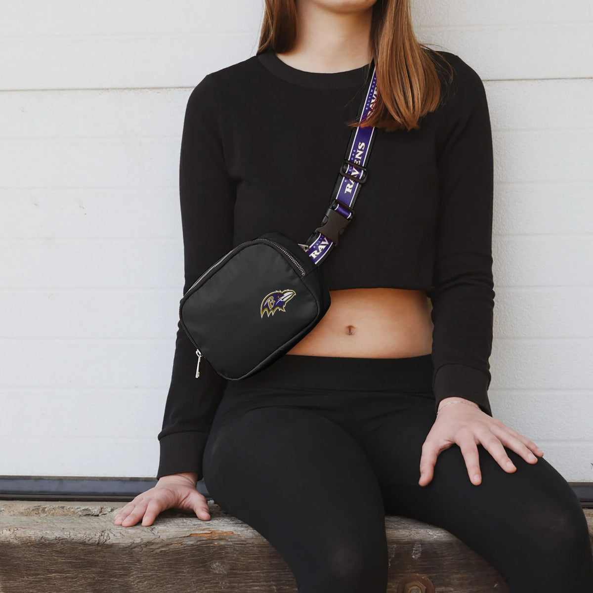 Person wearing a black sweatshirt and leggings with a black fanny pack featuring a logo.