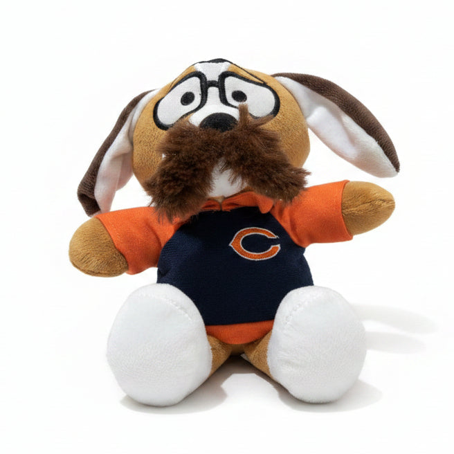 A plush dog toy wearing an orange and navy blue Chicago Bears jersey, sitting on a beige carpet against a beige wall.